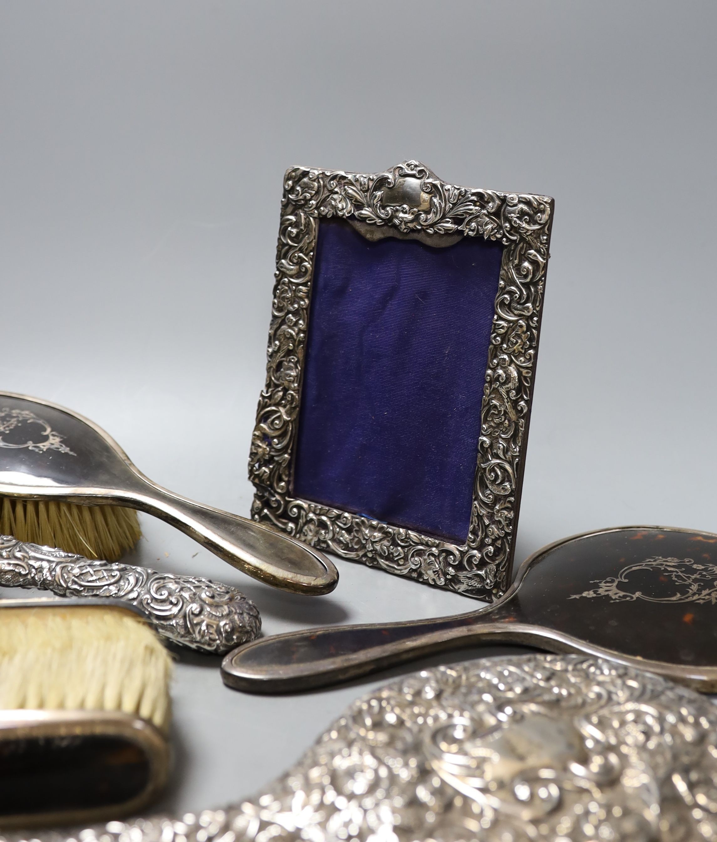 A George V silver and tortoiseshell mounted brush set and a tow similar embossed silver items(a.f.) and a silver mounted photograph frame.